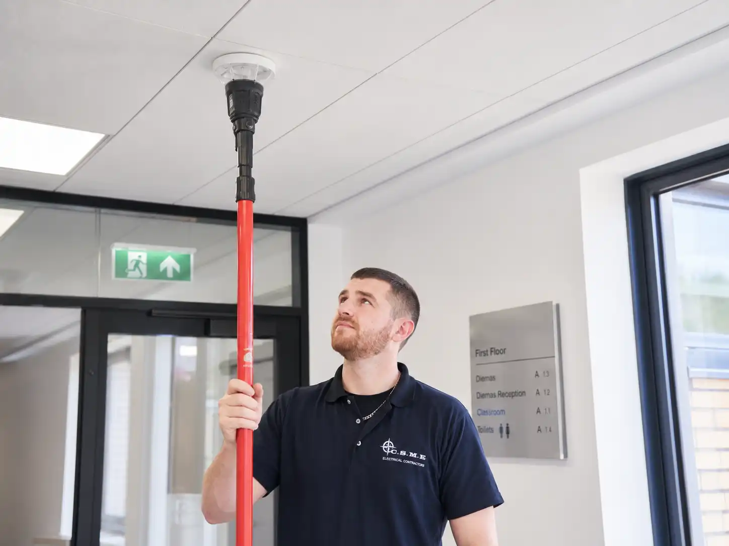 Connor testing an emergency light fitting at ceiling level